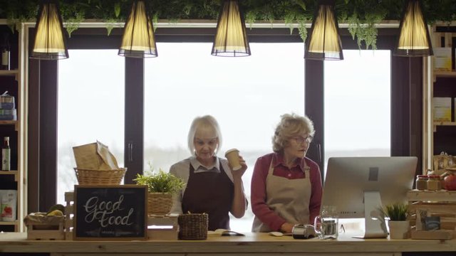 Wide shot of busy senior businesswomen standing at cash register of their shop and working 