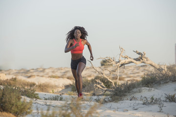Beautiful Black African American fitness athlete in the desert wearing a bright fitness outfit, running with dead tree branches and shrubs