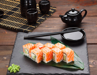 Salmon sushi roll on a stone plate and wooden background.