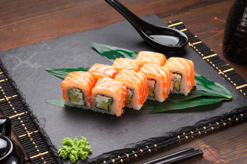 Salmon sushi roll on a stone plate and wooden background.