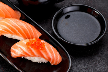 Salmon sushi with soy sauce on a black plate and dark concrete background.