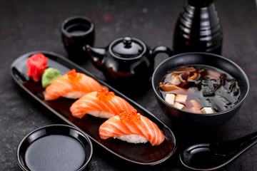 Japanese cuisine. Salmon sushi nigiri and miso soup on black plate a dark table.