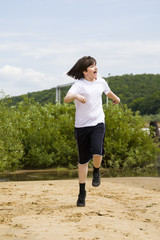 Happy teenager in white t-shirt runs on a sandy beach on a summe