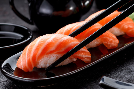 Japanese cuisine. Salmon sushi nigiri on a black plate with chopsticks.