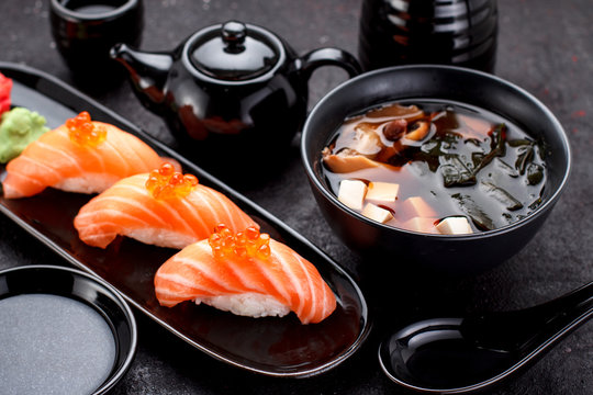 Japanese cuisine. Salmon sushi nigiri and miso soup on black plate a dark table.