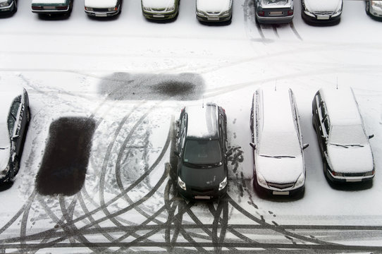 Ground parking cars after snowfall, view from above. Automobiles covered with snow, the traces of wheels and legs.