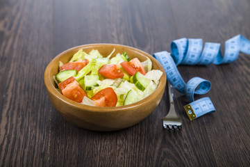 Salad in wooden bow, fork and measuring tape on a dark table clo