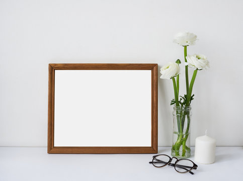 Interior poster mock up with horizontal wooden empty frame, bouquet of white flowers ranunculus, candle and glasses. Empty space for design presentation or your work © shurkin_son