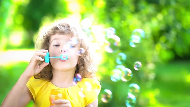 Happy child blowing soap bubbles in spring park. Kid having fun outdoors. Imagination and freedom concept. Slow motion from 120 fps