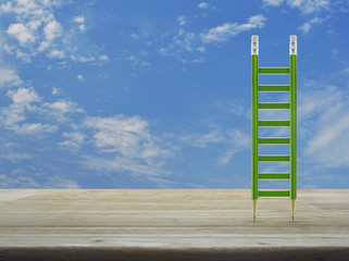 Green pencil ladder on wooden table over blue sky with white clouds, Business success concept