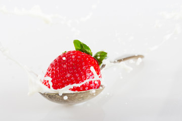 Strawberry falling into spoon full of cream