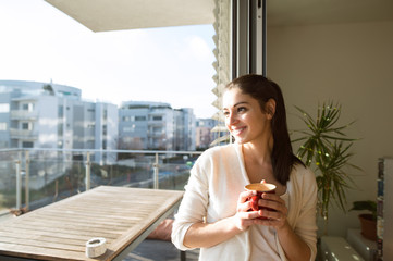Woman relaxing on balcony holding cup of coffee or tea - obrazy, fototapety, plakaty