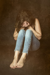 Naklejka premium Crying shy girl sitting on the ground. Curled up woman with face in hands