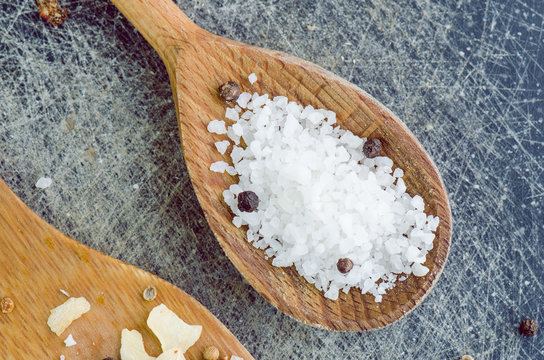 Mountain Stone Salt With Black Peppers In Wooden Spoon On Scratched Table Closeup
