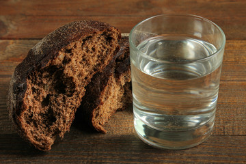 Glass of water and black bread on a wooden background. The concept of poverty.
