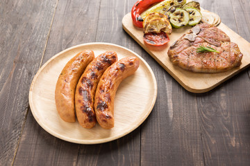 Sausages and grilled pork chop on the wooden background.