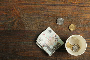 Money lying in a penny paper cup, on a wooden background. The concept of poverty.