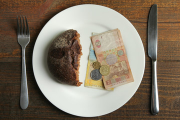 Piece of black bread with money lying on the plate. The concept of poverty.