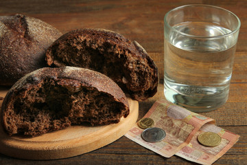 Glass of water, black bread and money on a wooden background. The concept of poverty.