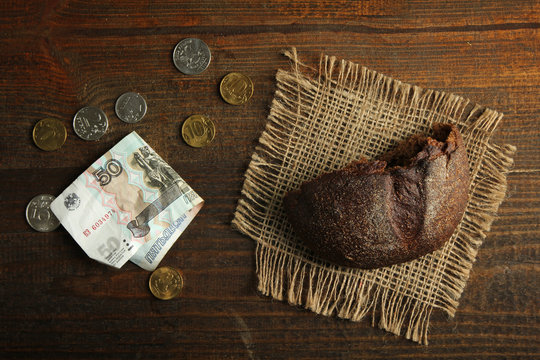 Piece of black bread with money on a wooden background. The concept of poverty.