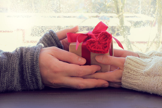 holiday greeting with a hint/ couple holds in hands gift with a heart symbol against the window