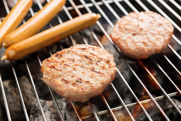 Hamburgers and sausages cooking over flames on grill