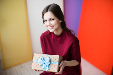 Happy woman holding a stylish gift with a blue ribbon on a colorful background.