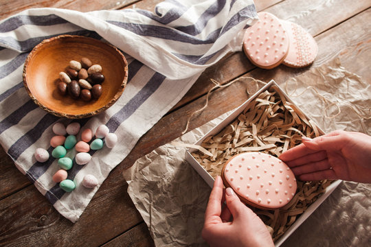 Hands put cookie into box with wooden shavings. Top view on woman preparing sweet Easter gifts, traditional treat. Homemade pastry, seasonal, holiday dessert concept