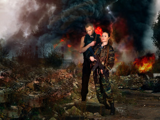 girl and man in military camouflage uniforms among the ruins of a fire in the background.