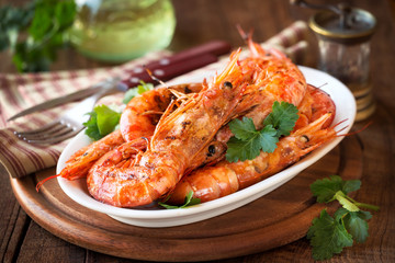 Grilled King prawns or shrimps with parsley on white plate on dark rustic wooden table