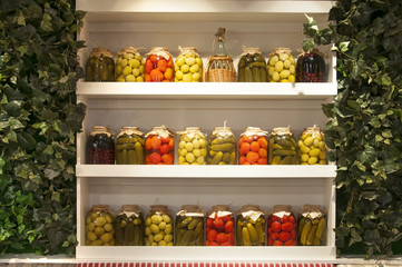 Collection of jars with canned vegetables on white shelves. Tomatoes and cucumbers in the winter.