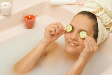 Obraz na płótnie Canvas girl in the bathtub apply cucumber slices to face with a towel on his head
