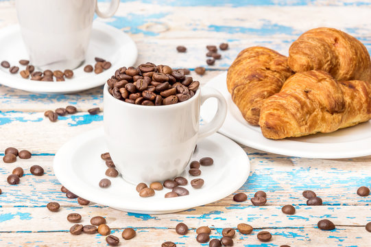 Two cup of coffee beans with croissants on the old wooden backgr