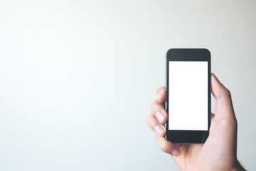 Mockup image of hand holding black mobile phone with blank white screen on white background room