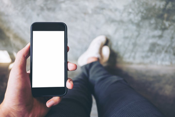 Mockup image of hand holding black mobile phone with blank white screen  with white canvas shoes on concrete polishing wall
