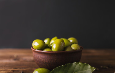 Green olives, bay leaf on a wooden board.  Olives on a black  background. Copyspace