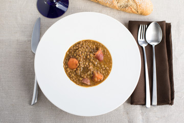 aerial view of white elegant plate with lentils stew, orange carrot, ham and sausage, typical...