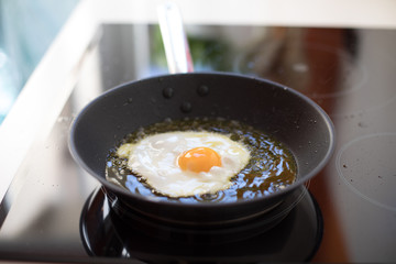 big silver metal dripping or frying pan or griddle cooking a fresh egg in hot oil on black cooker in white kitchen

