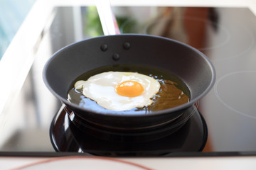 big silver metal dripping or frying pan or griddle cooking a fresh egg on black cooker in white kitchen
