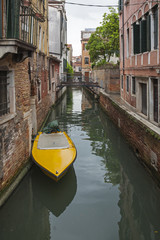 Fototapeta na wymiar Yellow boat anchored on canal in historical part of Venice