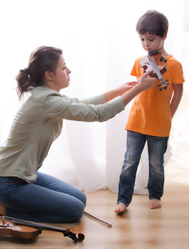 young musical teacher teaching little boy play violin, boy is lazy, refuses to play the violin. Opposing desires of mother and son.