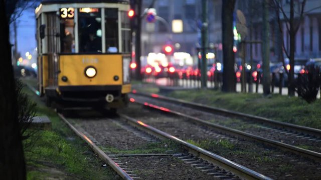 Tram che arriva di sera sullo sfondo passaggio pedonale e incrocio con gioco di luci della citt&agrave;