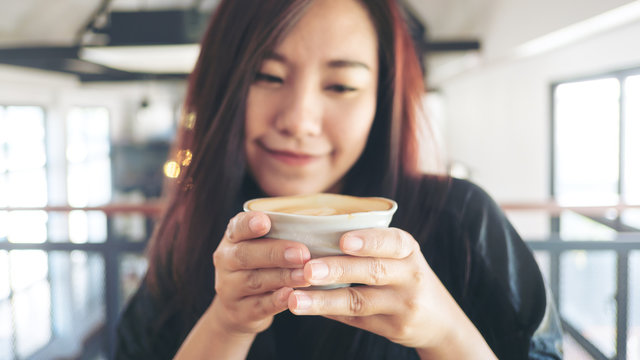 An asian woman holding and drinking hot coffee in the cafe