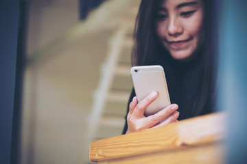 Beautiful Asian girl with smiley face using smart phone in modern cafe