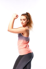 Portrait of a young athletic woman with a beautiful body relief. Teenager doing fitness. Sports as a hobby. The girl in a pink shirt and black tight sweat pants demonstrates arm muscles.