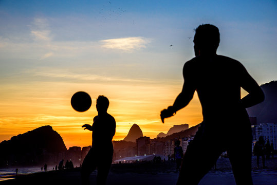 Beautiful sunset and silhouettes of men playing beach football at Copacabana beach, Rio de Janeiro, Brazil