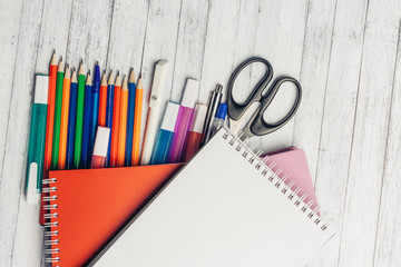 pens, markers and pencils lie on a wooden background and two notebooks