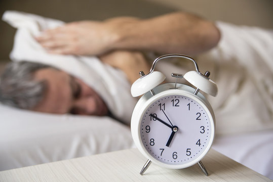 sleeping man disturbed by alarm clock early morning.  Sleepy mature man