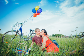 Happy young adult couple in love on the field. Two, man and woman have picnic, smiling and resting on the green grass.