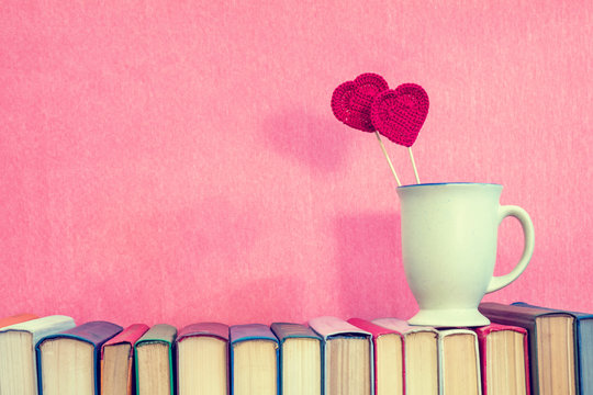 Valentines day concept. Cup with crochet hearts on books over pink background.